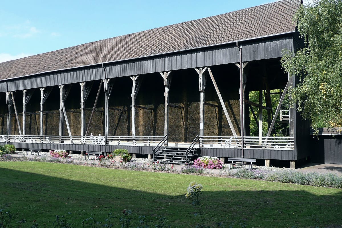 Historisches Gradierwerk aus dunklem Holz mit Schwarzdornwänden im Kurpark von Bad Salzdetfurth, davor Rasenfläche und Blumenbeete