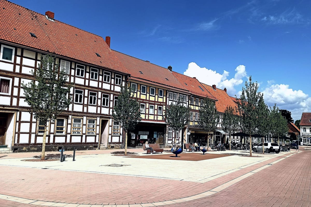 Buchholzmarkt in Bockenem mit sanierter Fachwerkhauszeile, jungen Bäumen und gepflastertem Platz unter blauem Himmel