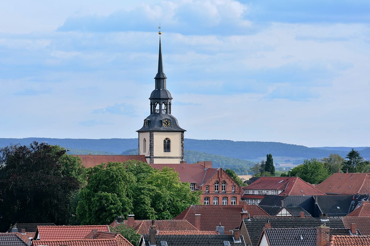 Stadtansicht von Elze an der Leine: Turm der Kirche St. Peter und Paul über roten Ziegeldächern, im Hintergrund bewaldete Hügel des Leineberglands