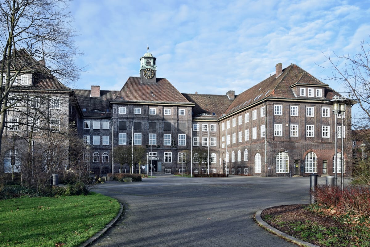 Rathaus der Stadt Lehrte am Rathausplatz: Verwaltungsgebäude hinter dem gepflasterten Platz mit Bäumen