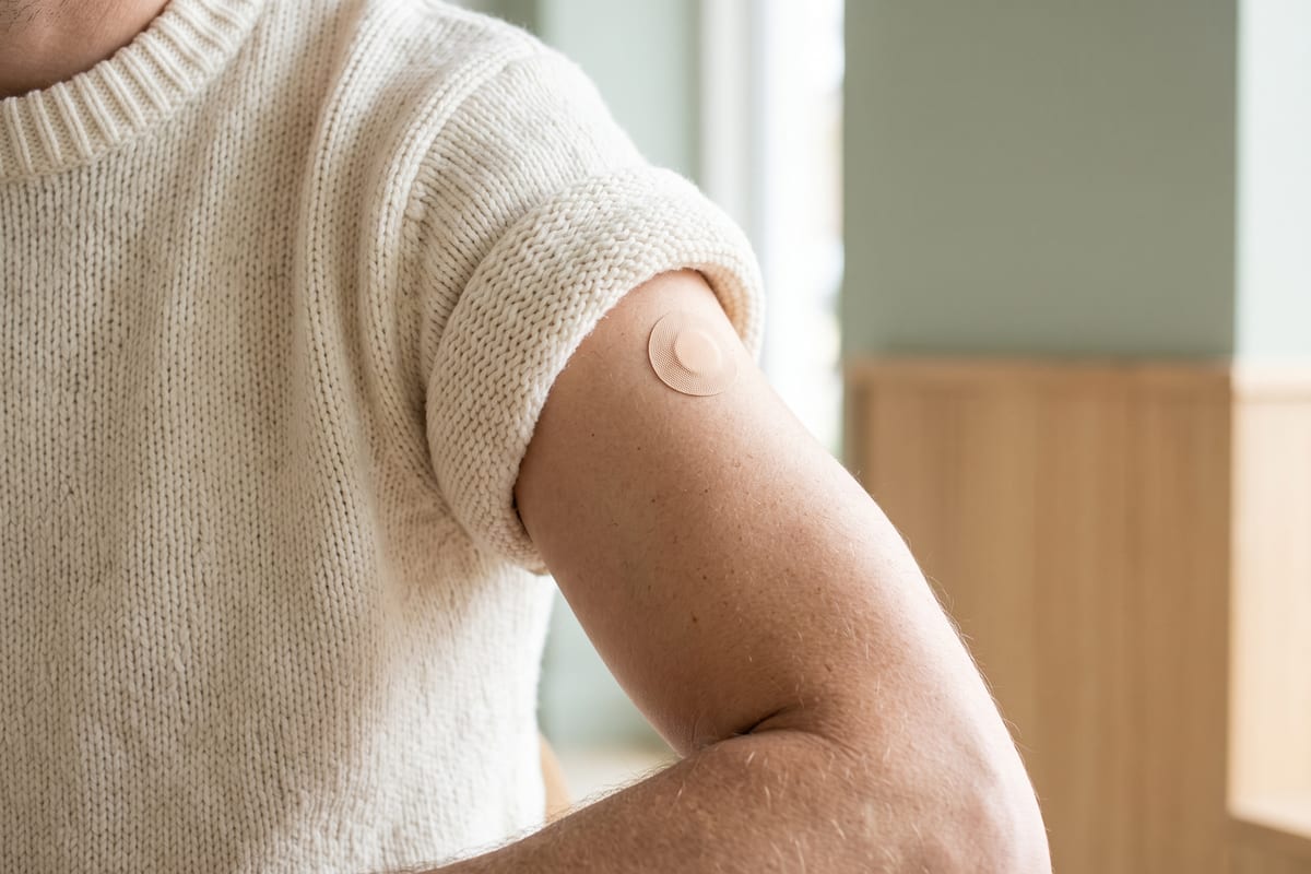 Oberarm mit hochgekrempeltem Ärmel eines cremefarbenen Strickpullovers und einem kleinen runden Pflaster